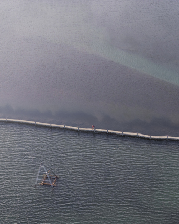 Aerial view of a narrow stone walkway extending into the sea with a person walking along it and a small wooden structure in the water near Premantura Istria County Croatia. Aerial view of a narrow stone walkway extending into the sea with a person walking along it and a small wooden structure in the water near Premantura Istria County Croatia.