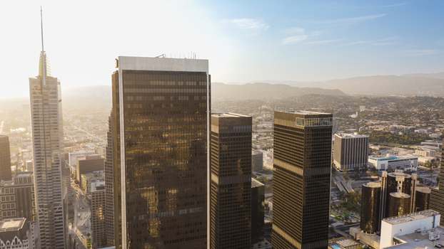 Aerial view of the Los Angeles skyline with modern glass skyscrapers reflecting golden hour sunlight urban sprawl and distant hills Los Angeles California United States.
