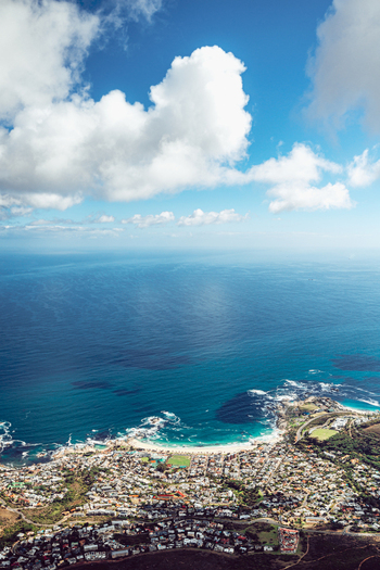 View of the coastal city and Camps Bay beach with turquoise ocean water under a blue sky with fluffy clouds in Cape Town Western Cape South Africa. View of the coastal city and Camps Bay beach with turquoise ocean water under a blue sky with fluffy clouds in Cape Town Western Cape South Africa.
