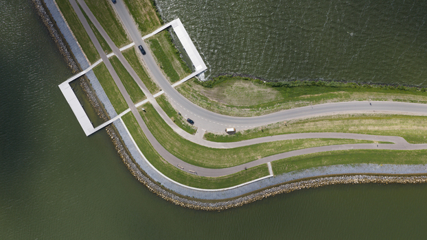 Aerial view of a winding dike road with green grass verges and a modern concrete structure extending into the water in Uitdam North Holland Netherlands.