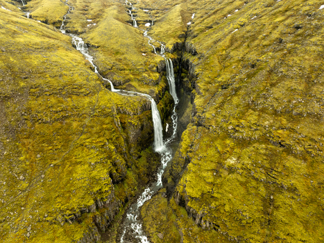 Aerial view of a cascading waterfall flowing through a deep moss covered rocky canyon in the Eastern Region of Iceland. Aerial view of a cascading waterfall flowing through a deep moss covered rocky canyon in the Eastern Region of Iceland.