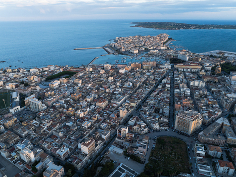 Aerial view of the Island of Ortigia and the historic city center with its dense rooftops and harbor under a soft blue sky in Syracuse Sicily Italy. Aerial view of the Island of Ortigia and the historic city center with its dense rooftops and harbor under a soft blue sky in Syracuse Sicily Italy.