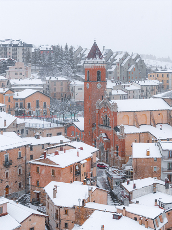 Aerial view of the snow covered town of Rivisondoli featuring the prominent red brick bell tower of the San Nicola di Bari church amidst winter rooftops in Rivisondoli Abruzzo Italy.