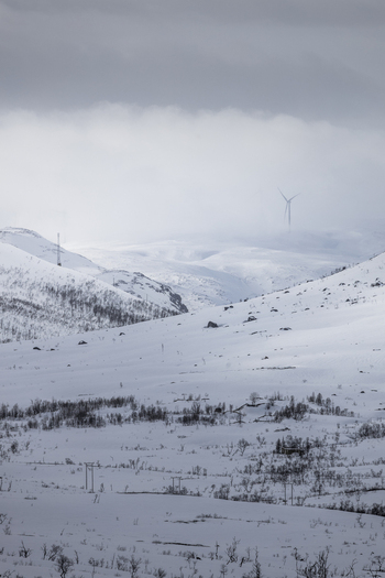 View of snow covered mountains with a wind turbine and power lines under a cloudy sky in Ersfjord Troms Norway. View of snow covered mountains with a wind turbine and power lines under a cloudy sky in Ersfjord Troms Norway.