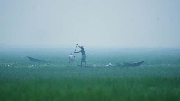 View of fishermen in small wooden boats on a misty river Bangladesh.