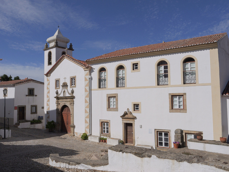 View of the historic church in the hilltop village of Marvao with white stone walls arched windows and bell tower under a clear blue sky in Marvao Portalegre District Portugal. View of the historic church in the hilltop village of Marvao with white stone walls arched windows and bell tower under a clear blue sky in Marvao Portalegre District Portugal.