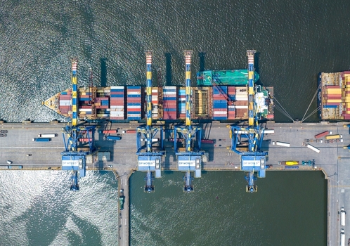 Aerial view of the Jawaharlal Nehru Port Authority terminal featuring a large container ship being loaded by gantry cranes with stacked shipping containers in Juna Sheva Maharashtra India. Aerial view of the Jawaharlal Nehru Port Authority terminal featuring a large container ship being loaded by gantry cranes with stacked shipping containers in Juna Sheva Maharashtra India.