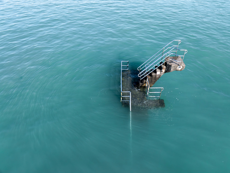 Aerial view of weathered stone steps with metal railings descend into the turquoise sea creating a stark contrast between the man made structure and the natural water Saint Malo Brittany France. Aerial view of weathered stone steps with metal railings descend into the turquoise sea creating a stark contrast between the man made structure and the natural water Saint Malo Brittany France.