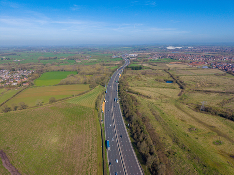 Aerial view of the M6 motorway stretching through the countryside with green fields hedgerows and scattered trees in Penkridge England United Kingdom. Aerial view of the M6 motorway stretching through the countryside with green fields hedgerows and scattered trees in Penkridge England United Kingdom.