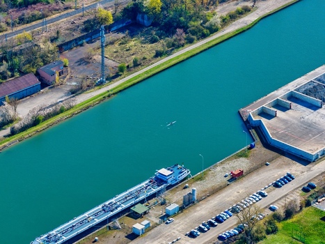 Aerial view of a turquoise canal reflecting the sky where an industrial barge rests near a parking lot Sausheim Grand Est France.