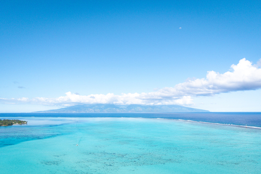 View of the turquoise lagoon and the mountainous island of Moorea under a clear blue sky in Moorea Maiao Windward Islands French Polynesia.