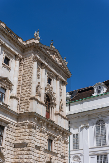 View of the ornate facade of the Hofburg Palace featuring classical statues and intricate architectural details under a clear blue sky in Vienna Vienna Austria. View of the ornate facade of the Hofburg Palace featuring classical statues and intricate architectural details under a clear blue sky in Vienna Vienna Austria.