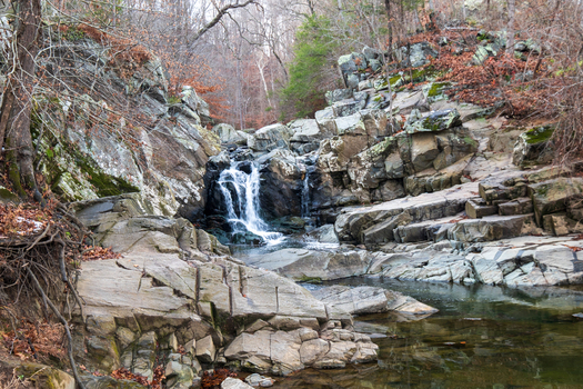 View of the cascading waterfall plunges down rugged grey rocky cliffs into a serene pool surrounded by leafless trees Scott s Run Virginia United States. View of the cascading waterfall plunges down rugged grey rocky cliffs into a serene pool surrounded by leafless trees Scott s Run Virginia United States.