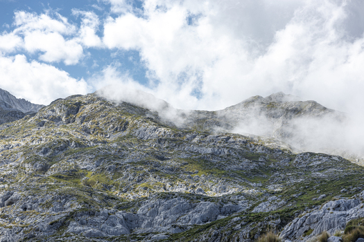View of rugged rocky mountains cloaked in ethereal mist and fluffy white clouds against a vibrant blue sky Picos de Europa Asturias Spain. View of rugged rocky mountains cloaked in ethereal mist and fluffy white clouds against a vibrant blue sky Picos de Europa Asturias Spain.