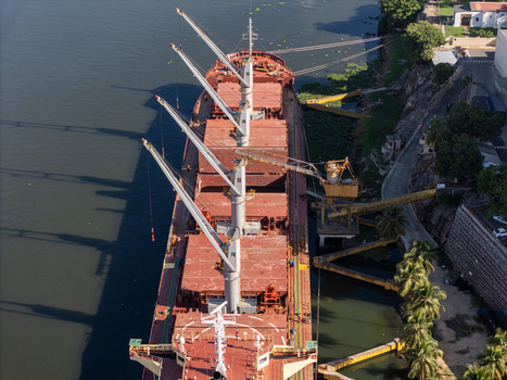 Aerial view of a large cargo ship docked at the port on the Rio Ozama featuring industrial cranes and the lush riverbank in Santo Domingo Santo Domingo Dominican Republic.