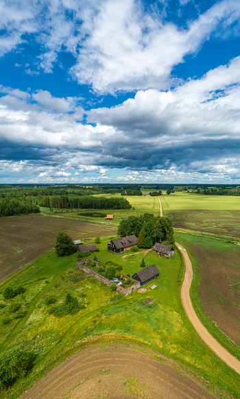 Aerial view of a rural farmstead with traditional buildings stone walls and surrounding green fields under a dramatic cloudy sky in Latvia. Aerial view of a rural farmstead with traditional buildings stone walls and surrounding green fields under a dramatic cloudy sky in Latvia.
