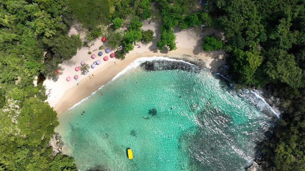 Aerial view of La Casita de Playa with turquoise waters sandy beach colorful umbrellas and lush green forest in Rio San Juan Maria Trinidad Sanchez Dominican Republic.