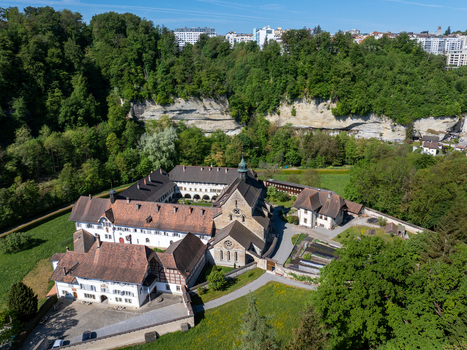 Aerial view of the historic La Maigrauge Abbey complex with its red tiled roofs and stone church nestled among lush green forests and limestone cliffs in Fribourg Fribourg Switzerland. Aerial view of the historic La Maigrauge Abbey complex with its red tiled roofs and stone church nestled among lush green forests and limestone cliffs in Fribourg Fribourg Switzerland.
