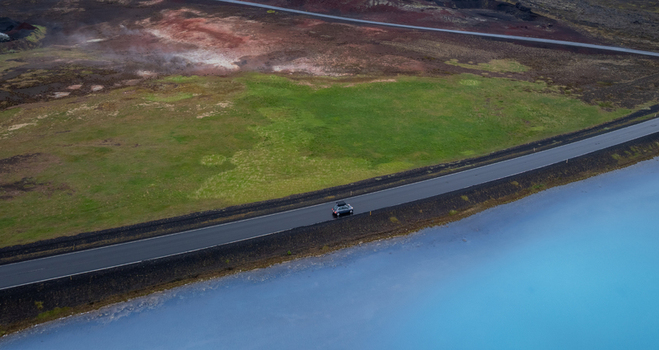 Aerial view of a car driving on a road through the geothermal landscape of Hverir with vibrant blue water and volcanic terrain in Reykjahlid Thingeyjarsveit Iceland. Aerial view of a car driving on a road through the geothermal landscape of Hverir with vibrant blue water and volcanic terrain in Reykjahlid Thingeyjarsveit Iceland.