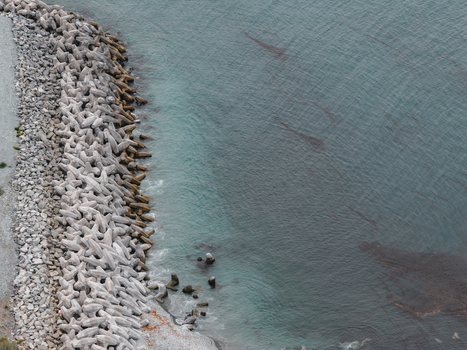 Aerial view of the concrete breakwater protecting the coastline with calm dark waters and kelp beds in Unalaska Alaska United States.