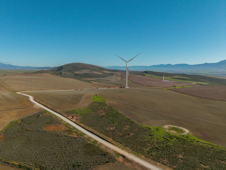 Aerial view of a large wind turbine standing in a rural landscape with rolling hills and a winding dirt road under a clear blue sky Swellendam Western Cape South Africa. Aerial view of a large wind turbine standing in a rural landscape with rolling hills and a winding dirt road under a clear blue sky Swellendam Western Cape South Africa.