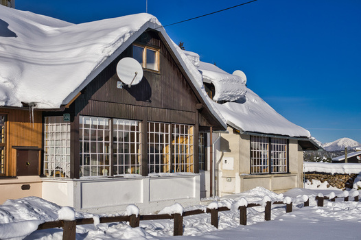 View of a snow laden cottage reveals a charming winter scene under a clear blue sky with a rustic fence dusted with snow in Donovaly Slovakia. View of a snow laden cottage reveals a charming winter scene under a clear blue sky with a rustic fence dusted with snow in Donovaly Slovakia.