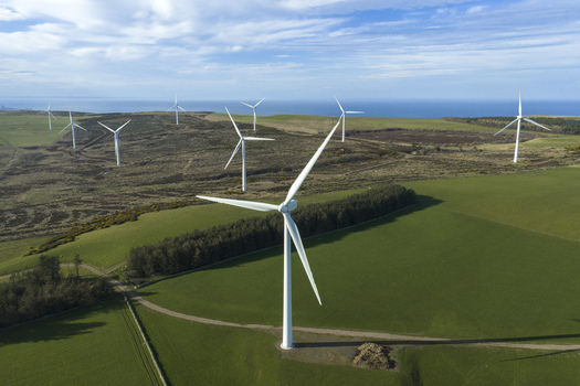 Aerial view of wind turbines of a windfarm standing on green rolling hills overlooking the sea under a blue sky Scotland United Kingdom. Aerial view of wind turbines of a windfarm standing on green rolling hills overlooking the sea under a blue sky Scotland United Kingdom.