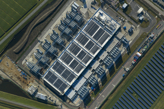 Aerial view of digital data center facility with solar panels on the roof and an adjacent solar farm under bright sunlight Netherlands. Aerial view of digital data center facility with solar panels on the roof and an adjacent solar farm under bright sunlight Netherlands.