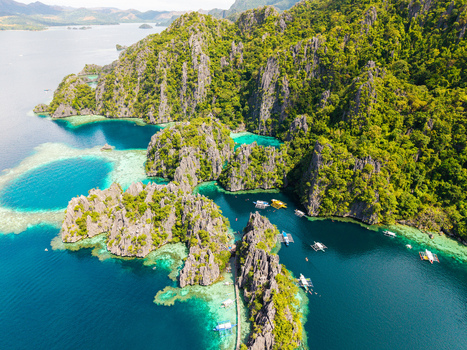 Aerial view of Twin Lagoon featuring turquoise waters surrounded by limestone cliffs and outrigger boats in Coron Mimaropa Philippines.