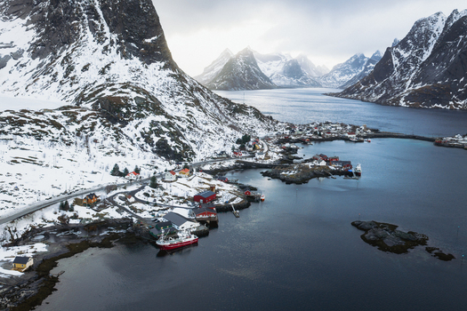Aerial view of Reinebringen Norway where snow dusted mountains meet the icy fjord casting long shadows over the quaint village below Reinebringen Nordland Norway.