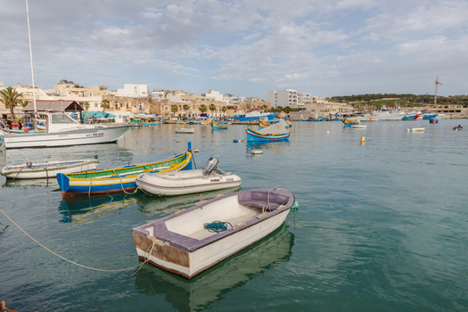 View of boats bobbing in the turquoise harbor contrasting with the aged buildings under a soft sky creating a tranquil scene Marsaxlokk Malta. View of boats bobbing in the turquoise harbor contrasting with the aged buildings under a soft sky creating a tranquil scene Marsaxlokk Malta.