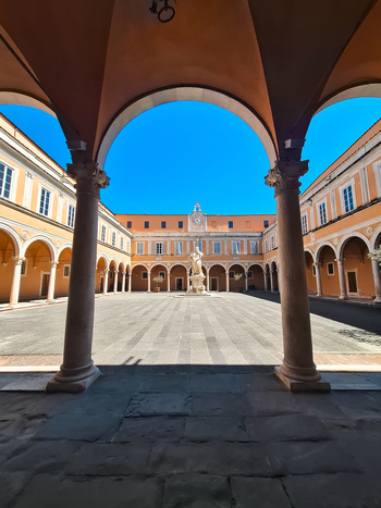 Pisa Italy 27 April 2026 View of the historic courtyard in Pisa Italy featuring elegant arched colonnades a central statue and warm sunlight under a clear blue sky. Pisa Italy 27 April 2026 View of the historic courtyard in Pisa Italy featuring elegant arched colonnades a central statue and warm sunlight under a clear blue sky.