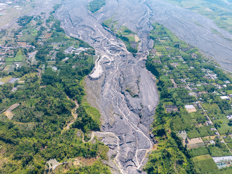 Aerial view of volcanic debris flow from Mount Semeru covering the landscape near Supiturang Village with ash deposits contrasting against green fields in Pronojiwo East Java Indonesia.