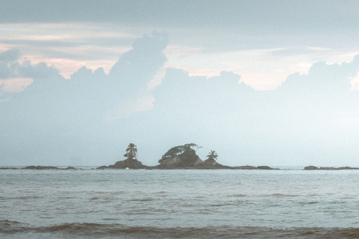 View of small rocky islands with palm trees rising from the ocean under a cloudy sky in Costa Rica.