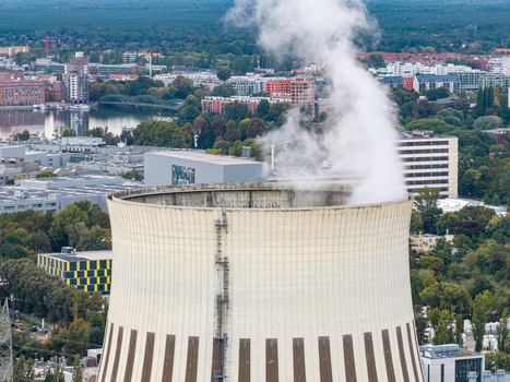 Aerial view of the Heizkraftwerk Reuter West cooling tower emitting steam surrounded by urban infrastructure lush trees and the Spree river in Berlin Berlin Germany.