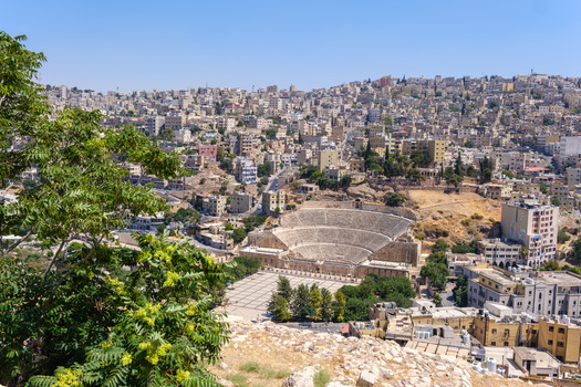 View of the historic Roman Theater nestled within the urban landscape of Amman featuring stone seating tiers and a large plaza in Amman Amman Governorate Jordan.