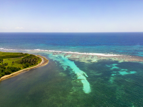 Aerial view of the turquoise coastline and coral reefs bordering the lush tropical landscape under a clear blue sky in Guanaja Bay Islands Department Honduras. Aerial view of the turquoise coastline and coral reefs bordering the lush tropical landscape under a clear blue sky in Guanaja Bay Islands Department Honduras.