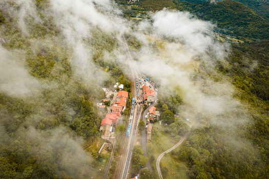 Aerial view of a train station nestled in the dense forests with a train on the tracks surrounded by mist and clouds in Buzet Istria County Croatia.