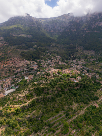 Aerial view of the historic village of Valldemossa with traditional stone houses nestled among lush green hills and the Tramuntana mountains Valldemossa Balearic Islands Spain.