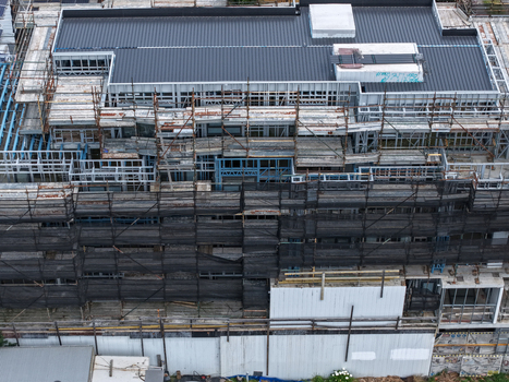 Aerial view of a large construction site featuring extensive scaffolding metal framing and a dark roof structure in Melbourne VIC Australia.