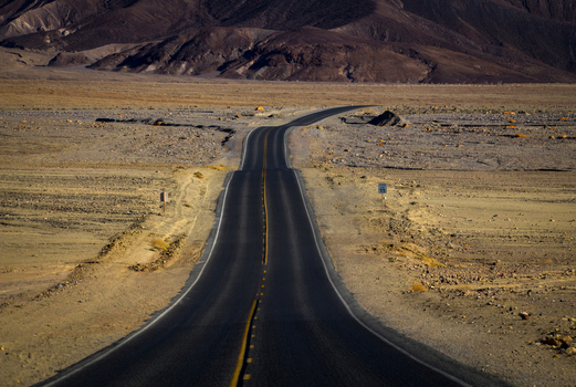View of a long winding asphalt road stretching through the arid desert landscape of Death Valley National Park with rugged mountains in the background Death Valley California United States.