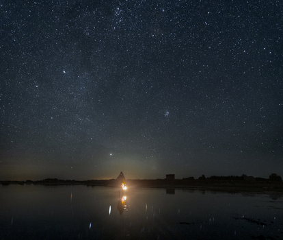 Laane County Estonia 06 September 2024 View of a person holding a light while standing in the shallow waters of Vormsi under a vast star filled night sky.