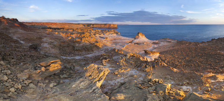 View of rugged limestone rock formations and weathered cliffs along the coastline under a clear blue sky during golden hour in Twelve Apostles Marine National Park Australia. View of rugged limestone rock formations and weathered cliffs along the coastline under a clear blue sky during golden hour in Twelve Apostles Marine National Park Australia.
