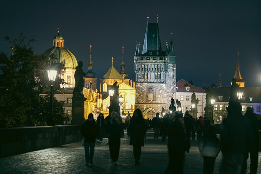 Prague Czechia 03 November 2021 View of the historic Charles Bridge at night with the illuminated Old Town Bridge Tower and silhouettes of people walking along the stone path. Prague Czechia 03 November 2021 View of the historic Charles Bridge at night with the illuminated Old Town Bridge Tower and silhouettes of people walking along the stone path.