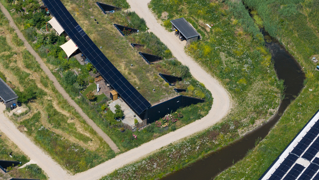 Aerial view of modern earth sheltered houses with green roofs and integrated solar panels surrounded by lush vegetation and a small canal in Almere Flevoland Netherlands. Aerial view of modern earth sheltered houses with green roofs and integrated solar panels surrounded by lush vegetation and a small canal in Almere Flevoland Netherlands.