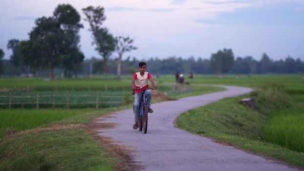 View of a young man riding a bicycle on a rural path Bangladesh.