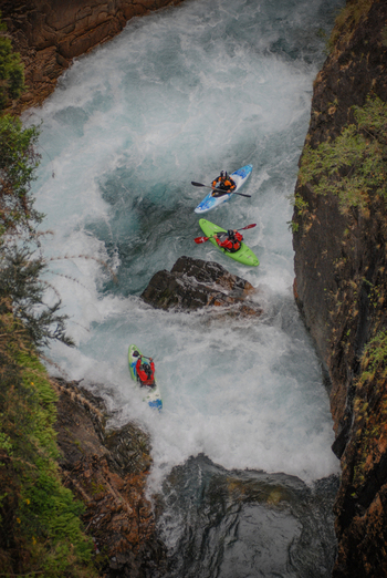 View of kayakers navigating the white water rapids of Rio Manso through a narrow rocky canyon with lush vegetation San Carlos de Bariloche Rio Negro Argentina. View of kayakers navigating the white water rapids of Rio Manso through a narrow rocky canyon with lush vegetation San Carlos de Bariloche Rio Negro Argentina.