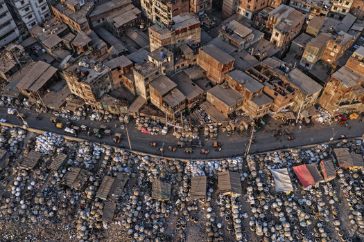 Aerial view of the Buriganga River bank featuring dense urban housing narrow streets with traffic and goods stored in sacks along the waterfront in Dhaka Dhaka Division Bangladesh. Aerial view of the Buriganga River bank featuring dense urban housing narrow streets with traffic and goods stored in sacks along the waterfront in Dhaka Dhaka Division Bangladesh.
