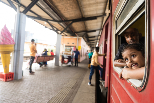 Sri Lanka 06 February 2026 View of a young girl looking out of a red train window at a railway station platform with a giant ice cream cone statue.