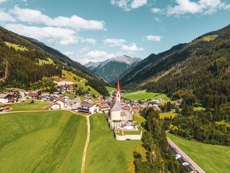 Aerial view of the village of Muhlwald featuring its church with a red spire surrounded by lush green alpine meadows and mountain peaks in Muhlwald Trentino Alto Adige Italy. Aerial view of the village of Muhlwald featuring its church with a red spire surrounded by lush green alpine meadows and mountain peaks in Muhlwald Trentino Alto Adige Italy.